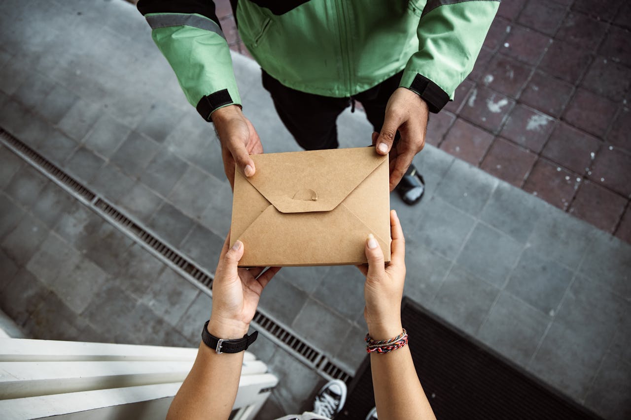 Close-up of hands exchanging a brown envelope outdoors on a pavement scene.